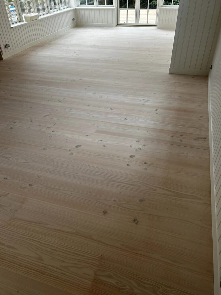 Lyst trægulv i solrig stue med store vinduer